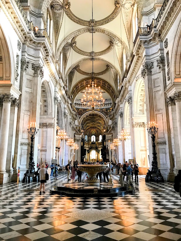 Interior nave of St Paul’s Cathedral in London with marble columns, chandeliers, and patterned floor